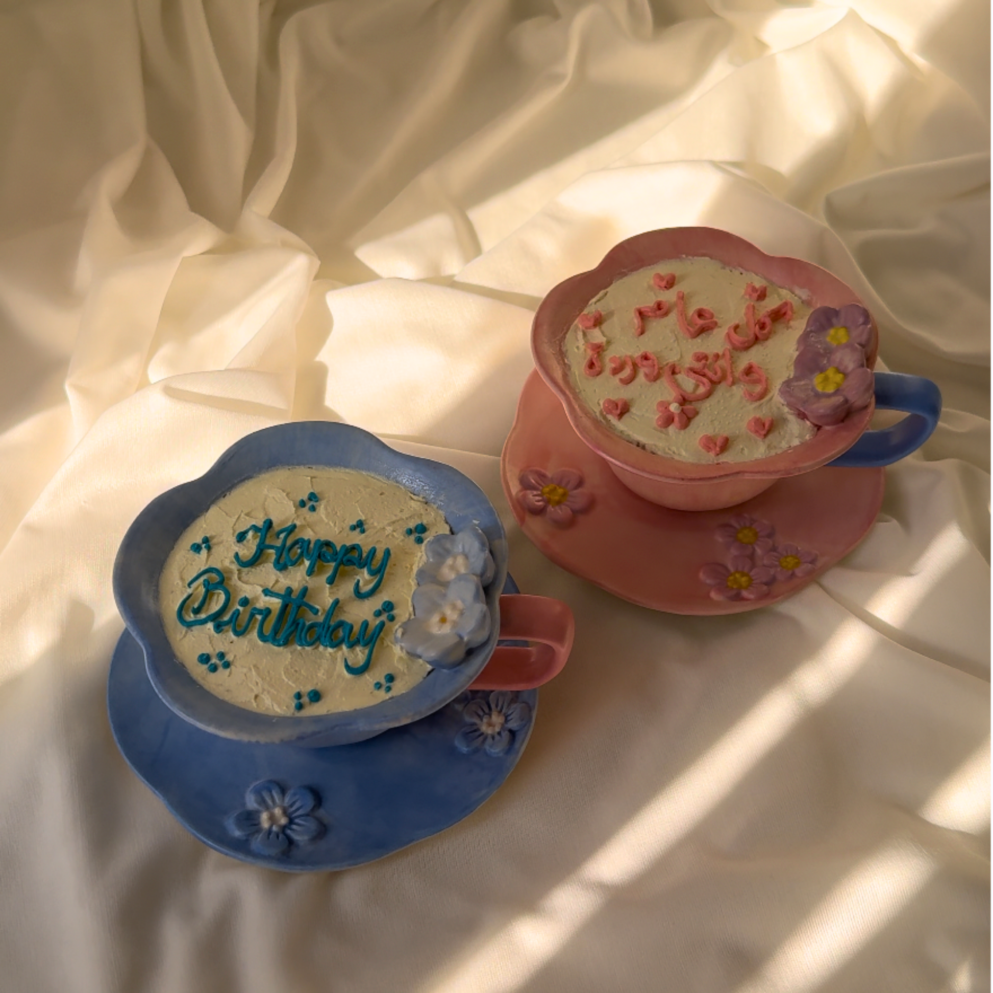 Two decorative teacups with 'Happy Birthday' text on a light fabric background