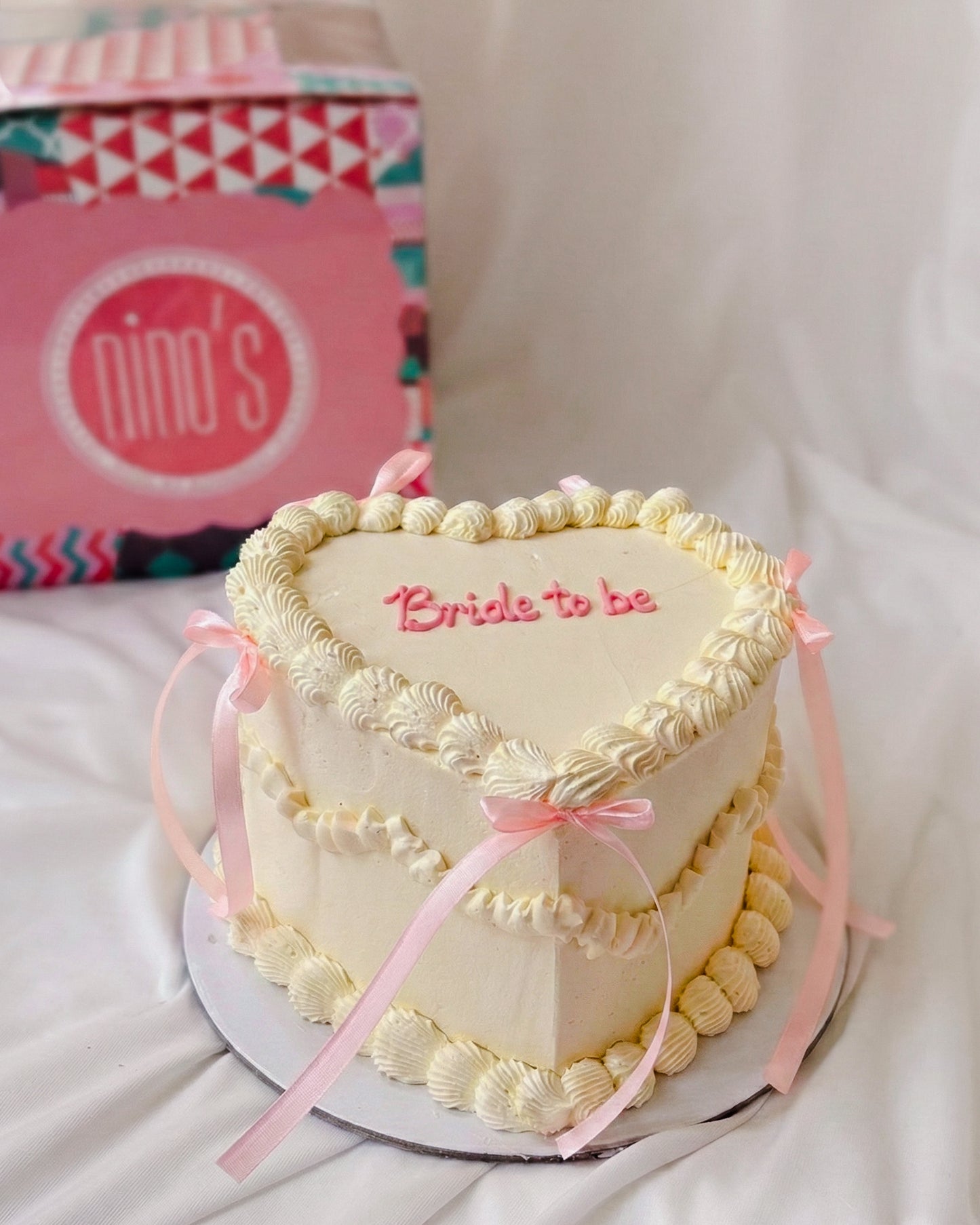 Heart-shaped cake with 'Bride to be' text, pink ribbons, and a pink box labeled 'nino's' in the background.