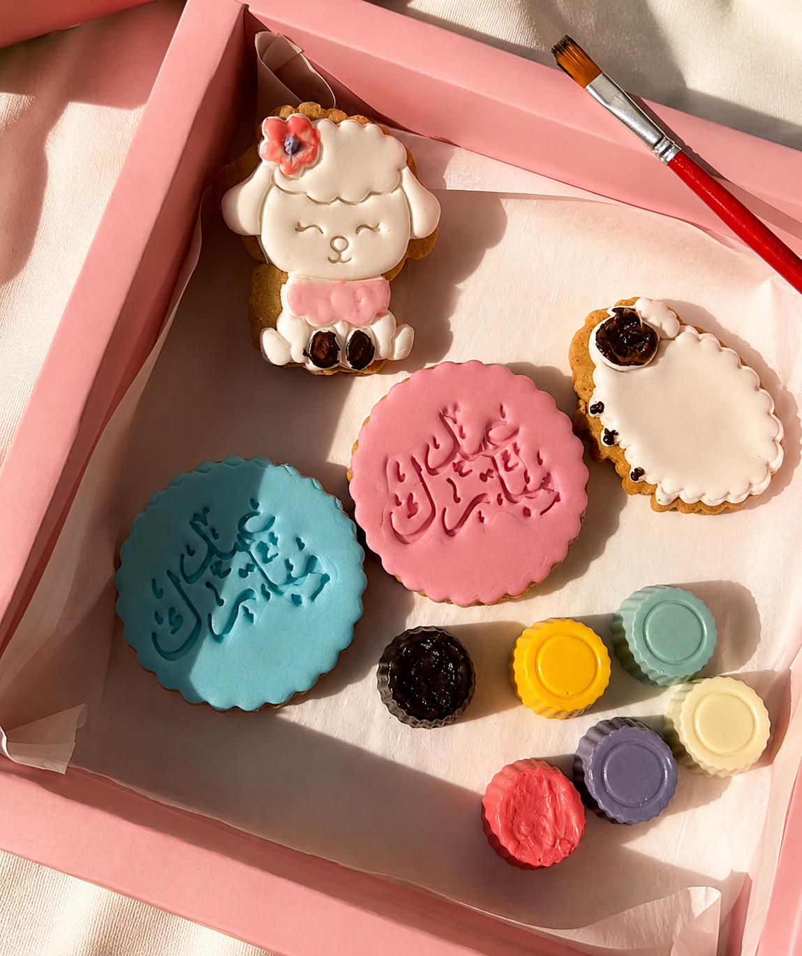 Decorative cookies with Arabic text in a pink box on a light background