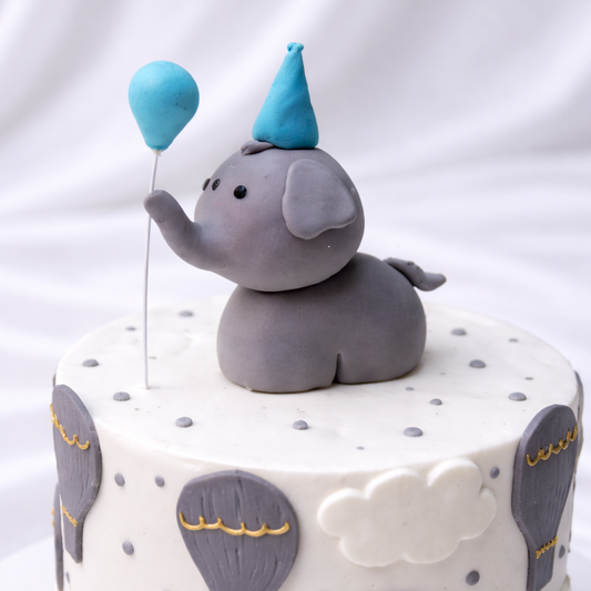Cake with elephant topper and blue balloons on a white background