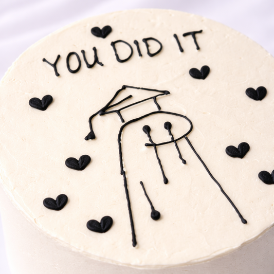 Graduation-themed cake with 'You Did It' text and a stick figure wearing a cap on a white background