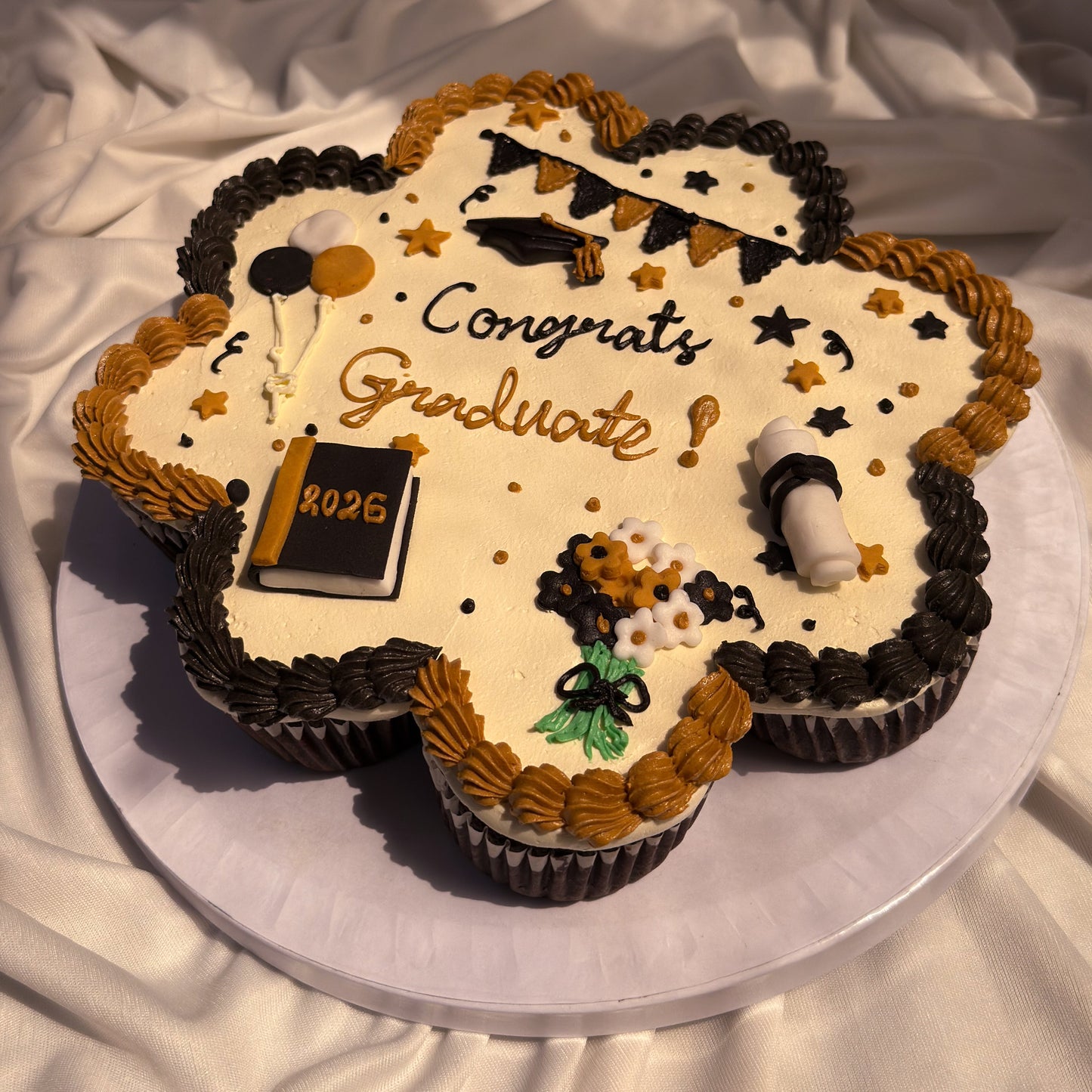 Graduation-themed cupcake with 'Congrats Graduate 2026' text on a white fabric background