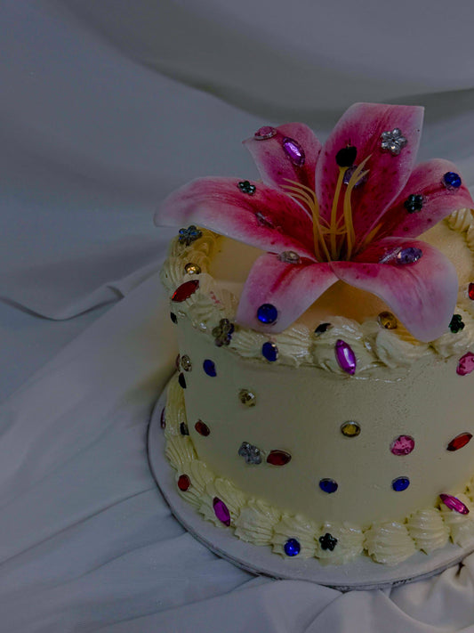 Decorative cake with a pink flower and colorful gemstones on a white background