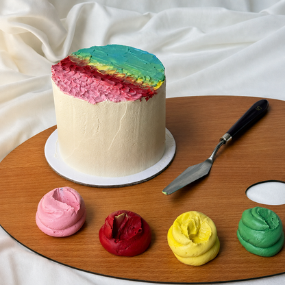 Colorful cake with rainbow frosting on a wooden palette with frosting samples and a spatula.