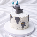 Small round cake with elephant topper and hot air balloon decorations on a white background