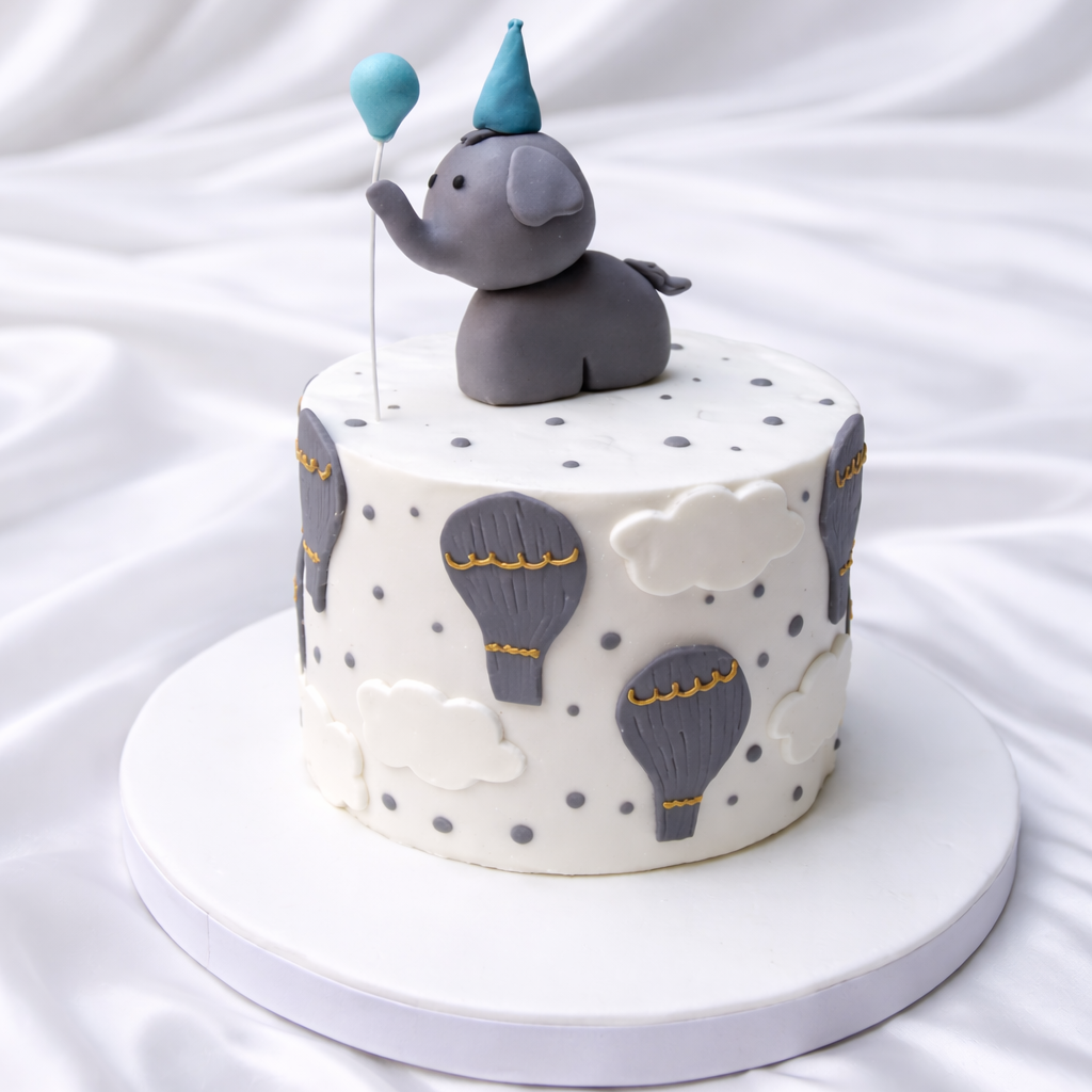 Small round cake with elephant topper and hot air balloon decorations on a white background