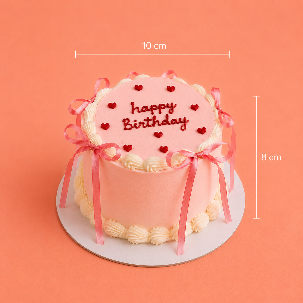 A pink frosted birthday cake with red heart decorations and 'happy Birthday' written on top, shown on a white round board against a peach background with dimension lines indicating 10 cm width and 8 cm height.