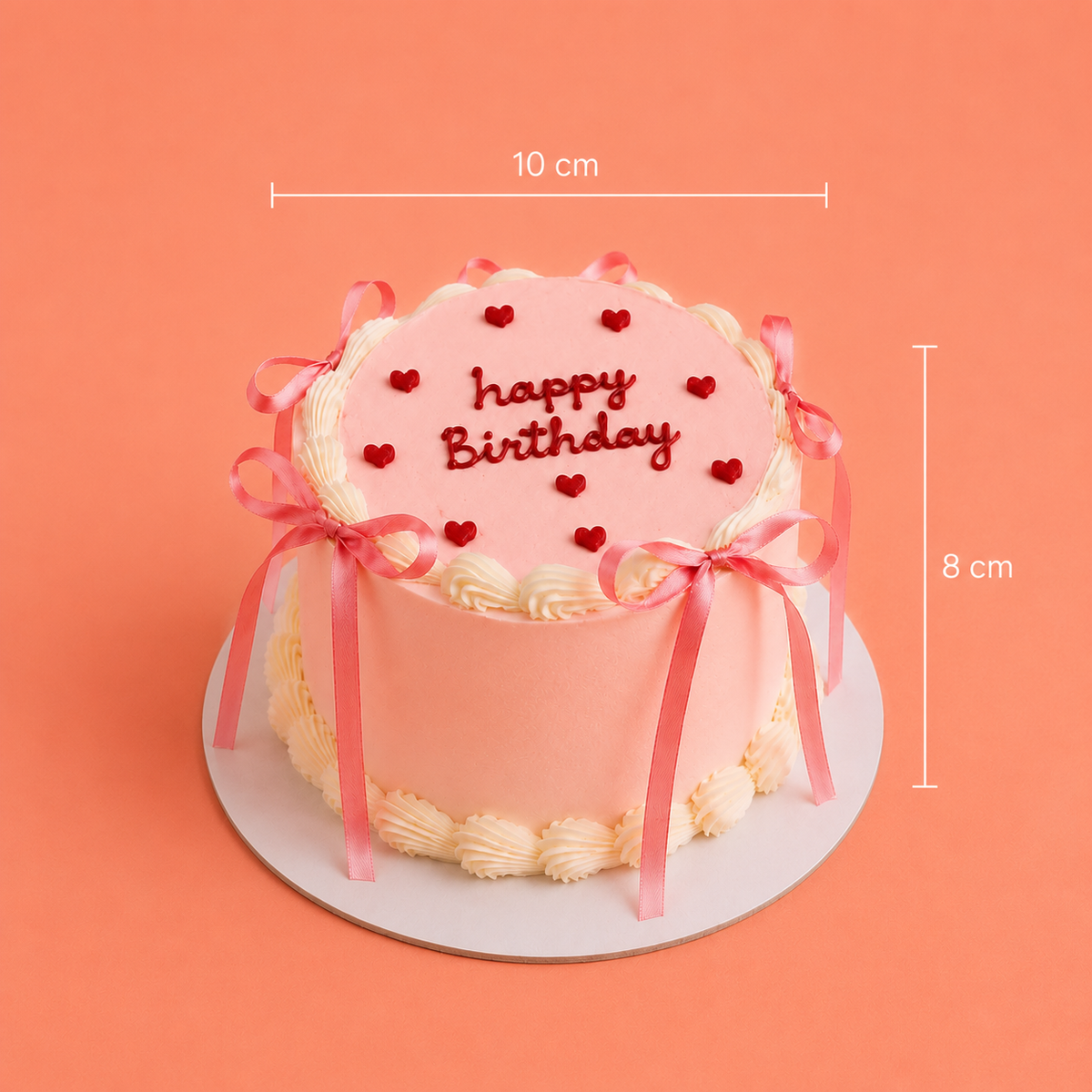 A pink frosted birthday cake with red heart decorations and 'happy Birthday' written on top, shown on a white round board against a peach background with dimension lines indicating 10 cm width and 8 cm height.