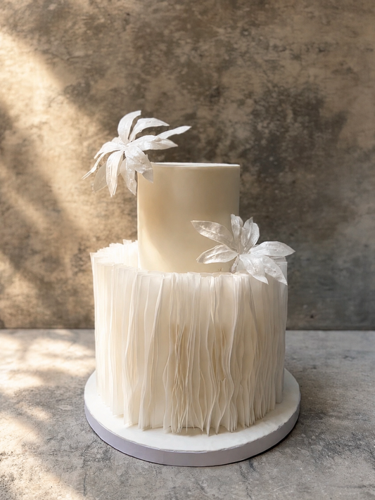 Two-tiered wedding cake with feathered bottom tier and floral decorations on a textured surface.