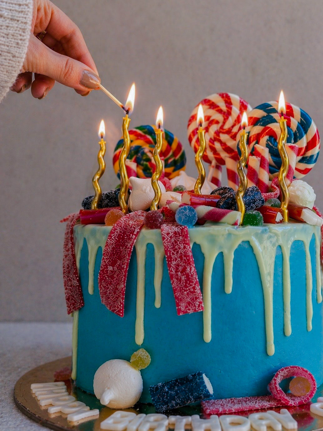 Colorful cake with candy decorations and lit candles on a neutral background
