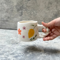Hand holding a ceramic mug with floral designs on a gray surface