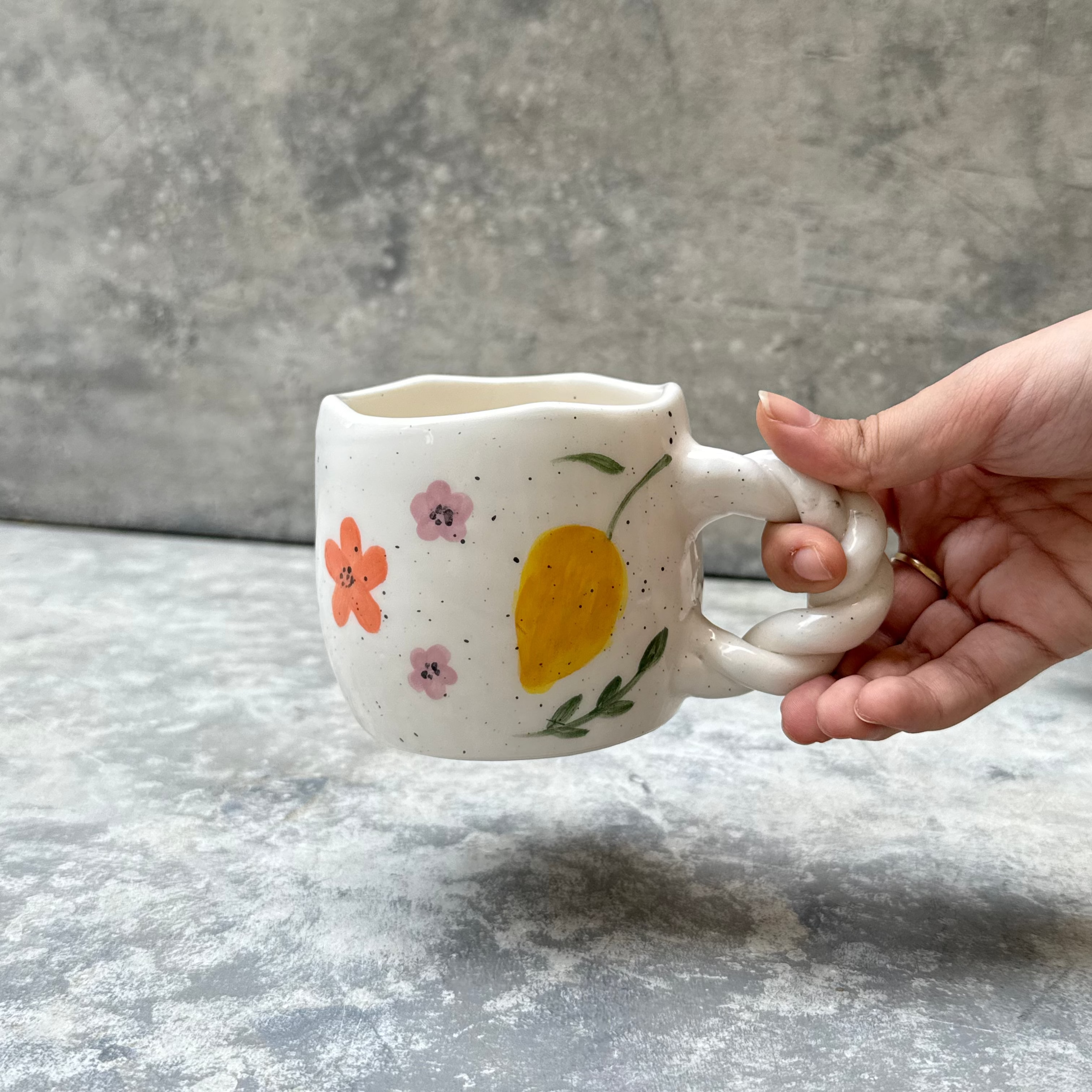 Hand holding a ceramic mug with floral designs on a gray surface