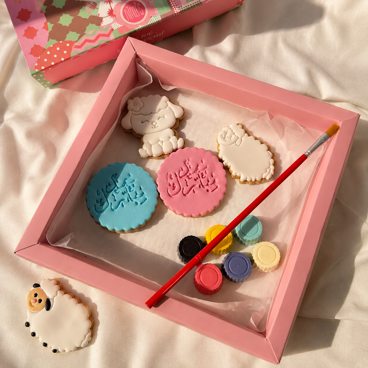 Decorative cookies with paintbrush and colors in a pink box on a light background