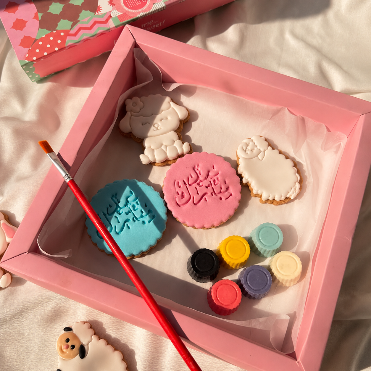 Decorative cookie set with pink box, paintbrush, and colorful paint pots on a light background