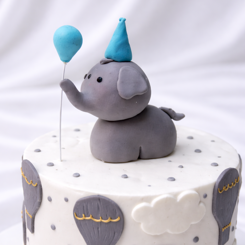Cake with elephant topper and blue balloons on a white background