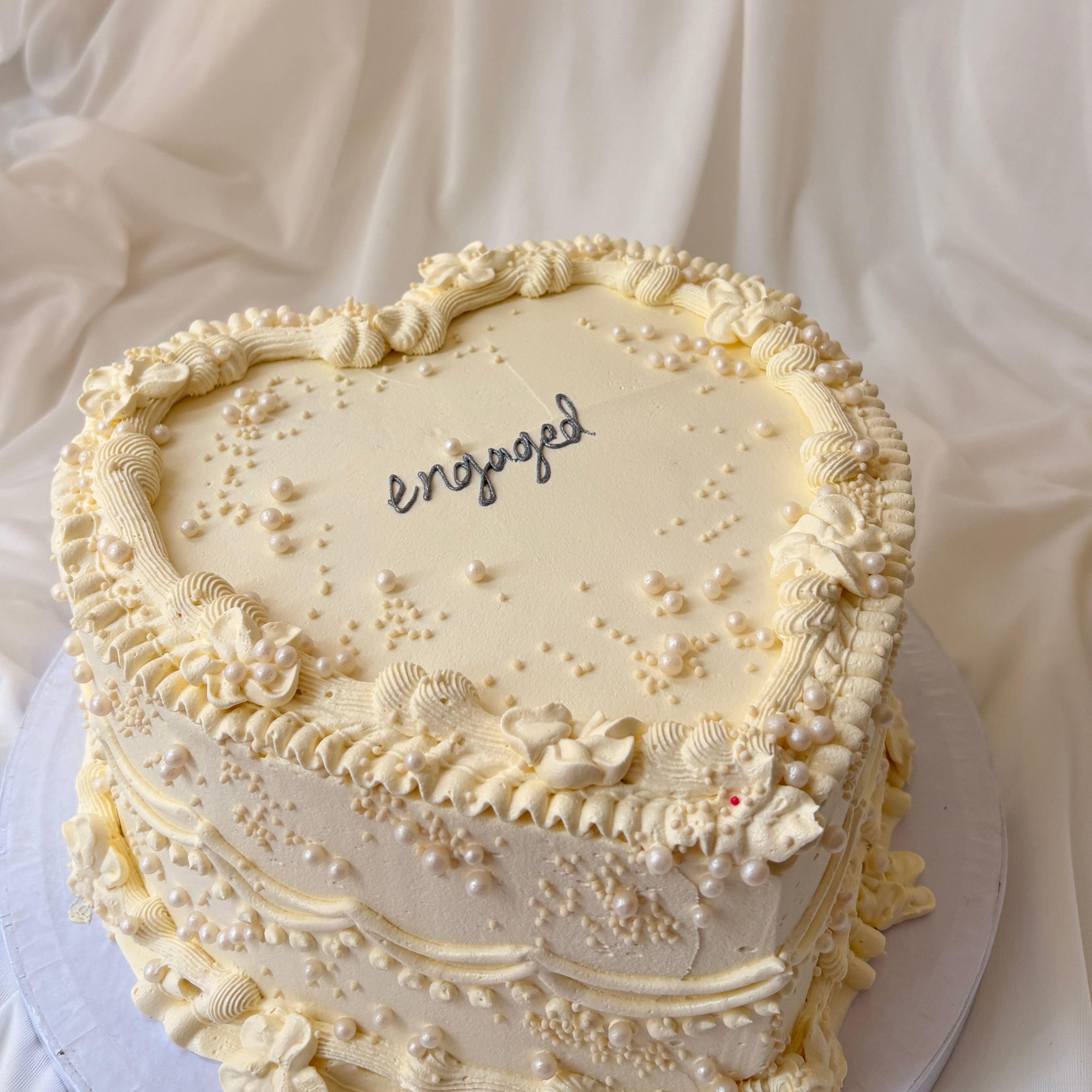 Heart-shaped cake with 'engaged' text on a white fabric background