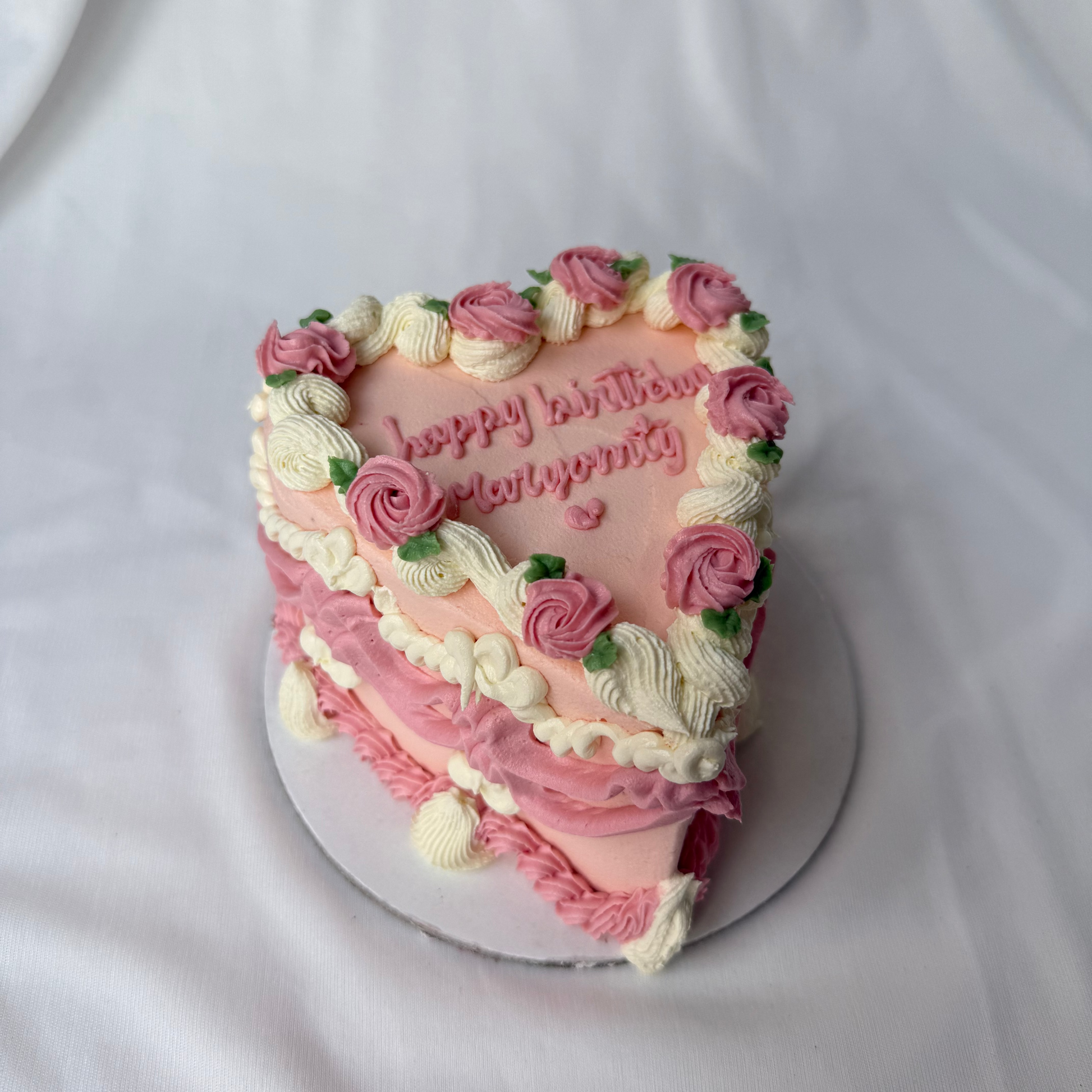 Heart-shaped birthday cake with pink and white frosting, decorated with flowers on a white background.
