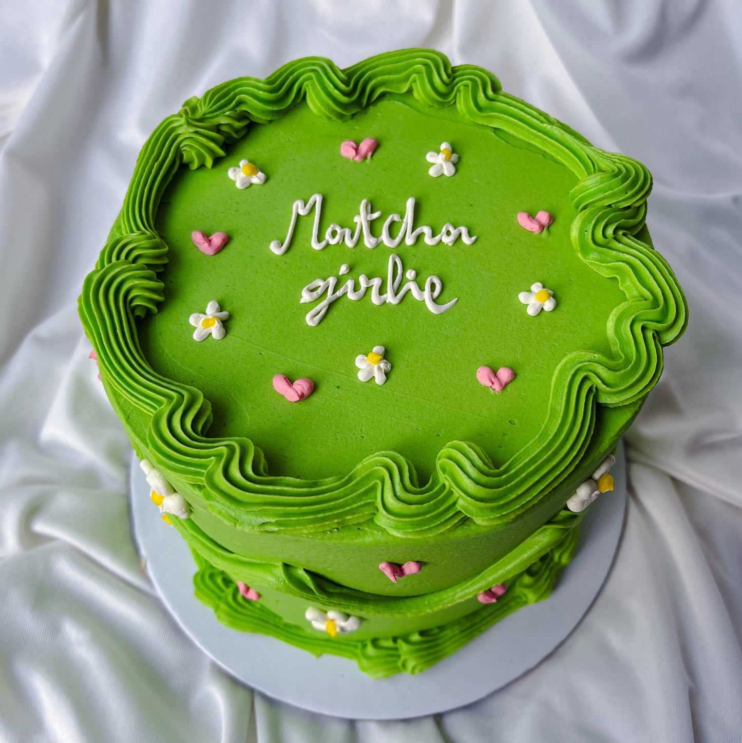 Green cake with decorative frosting and small flowers on a white fabric background