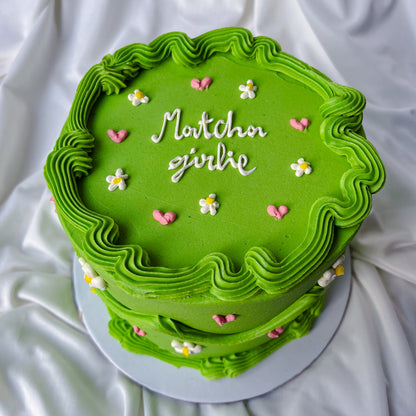 Green cake with decorative frosting and small flowers on a white fabric background