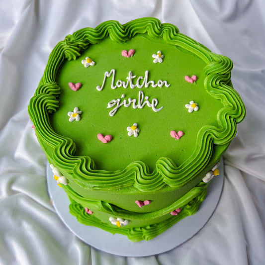 Green cake with decorative frosting and small flowers on a white fabric background