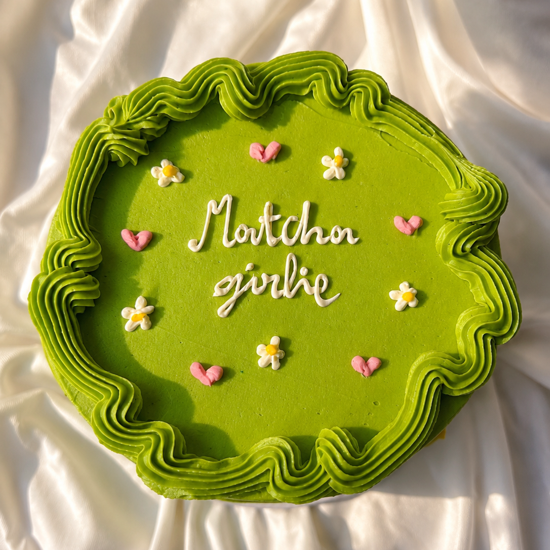 Green cake with decorative text and flowers on a white fabric background