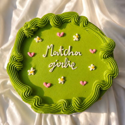 Green cake with decorative text and flowers on a white fabric background