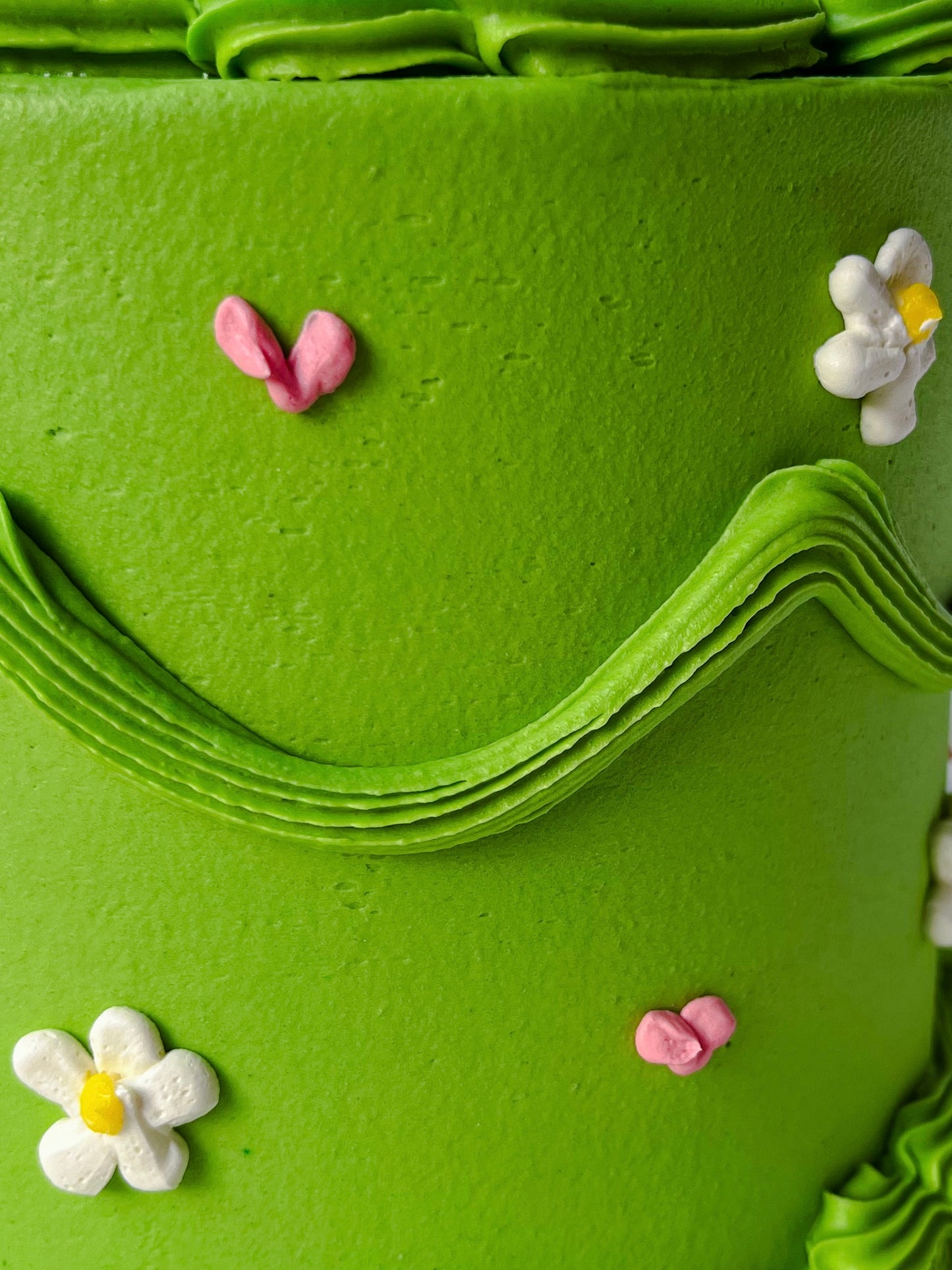 Close-up of a green cake with decorative flowers and butterflies.
