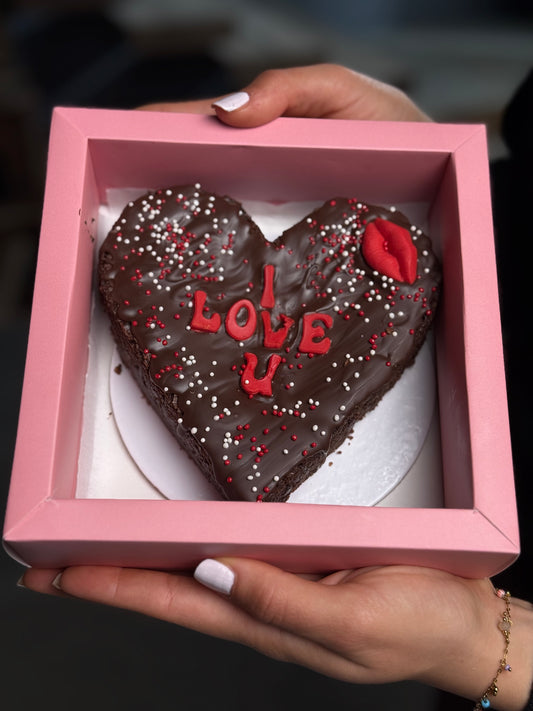 Heart-shaped chocolate cake with 'I LOVE U' chocolate text in a pink box held by a person.
