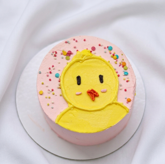Little Chick Cake decorated with cute yellow chick face and colorful sprinkles on pastel pink frosting