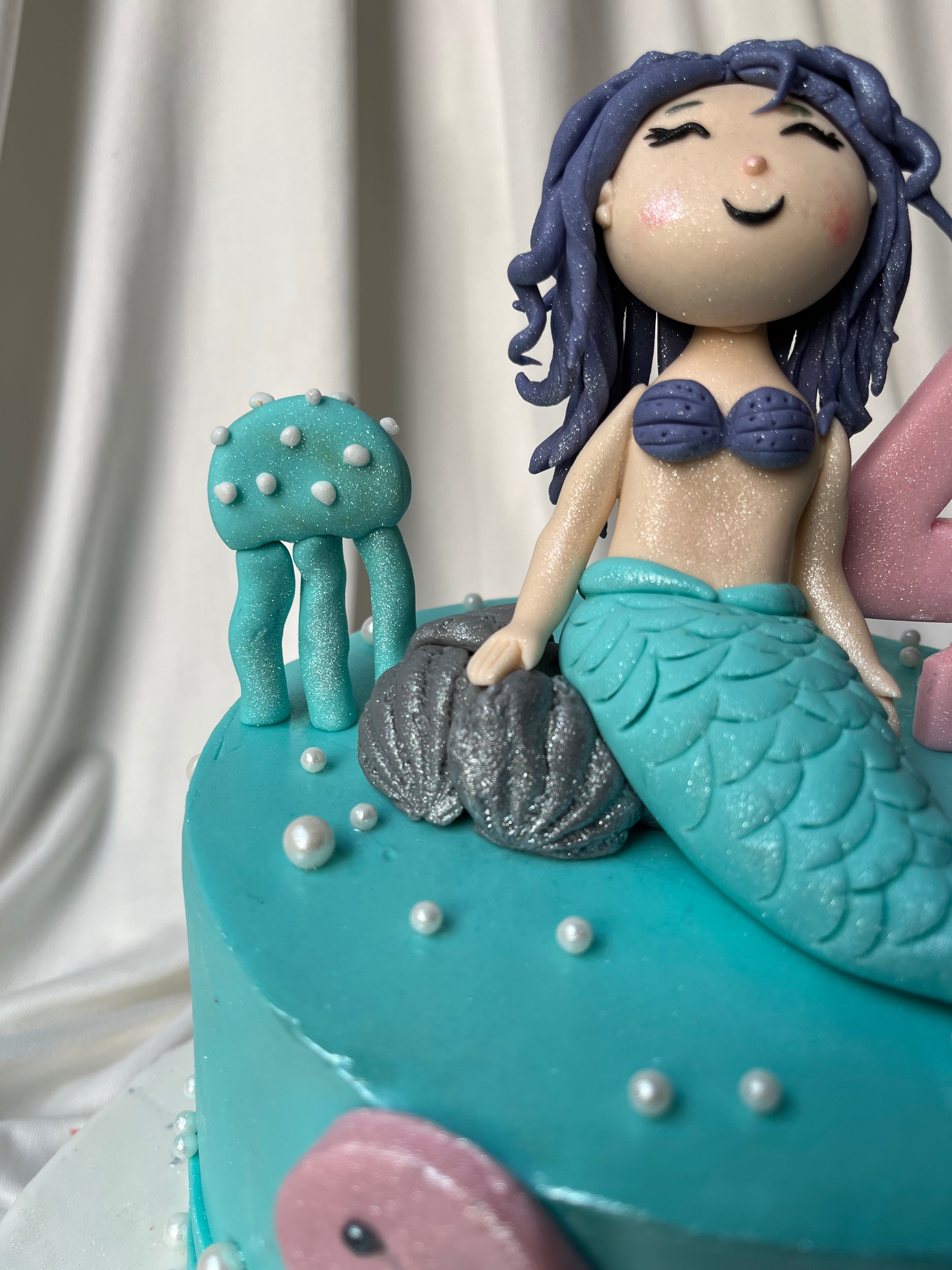 Mermaid-themed cake with a fondant mermaid and decorations on a white background