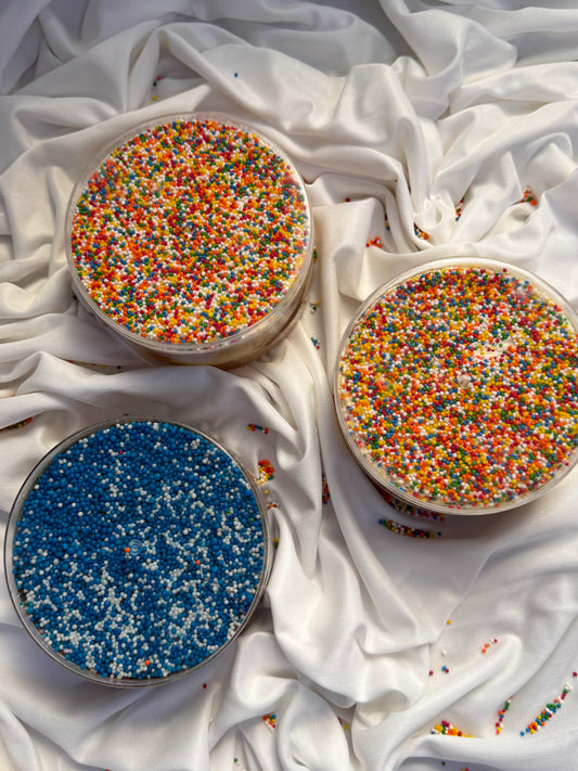 Three round containers filled with colorful sprinkles on a white fabric background