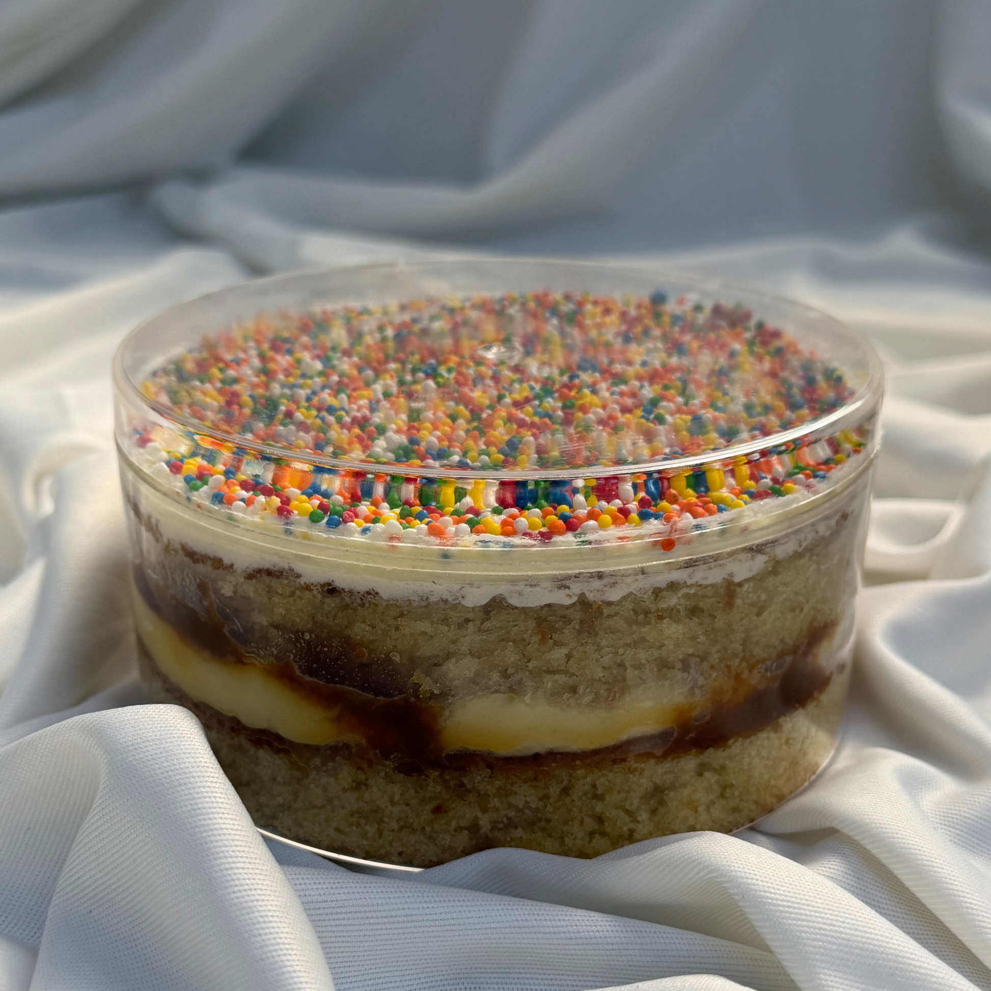 Small cake with colorful sprinkles on a white fabric background