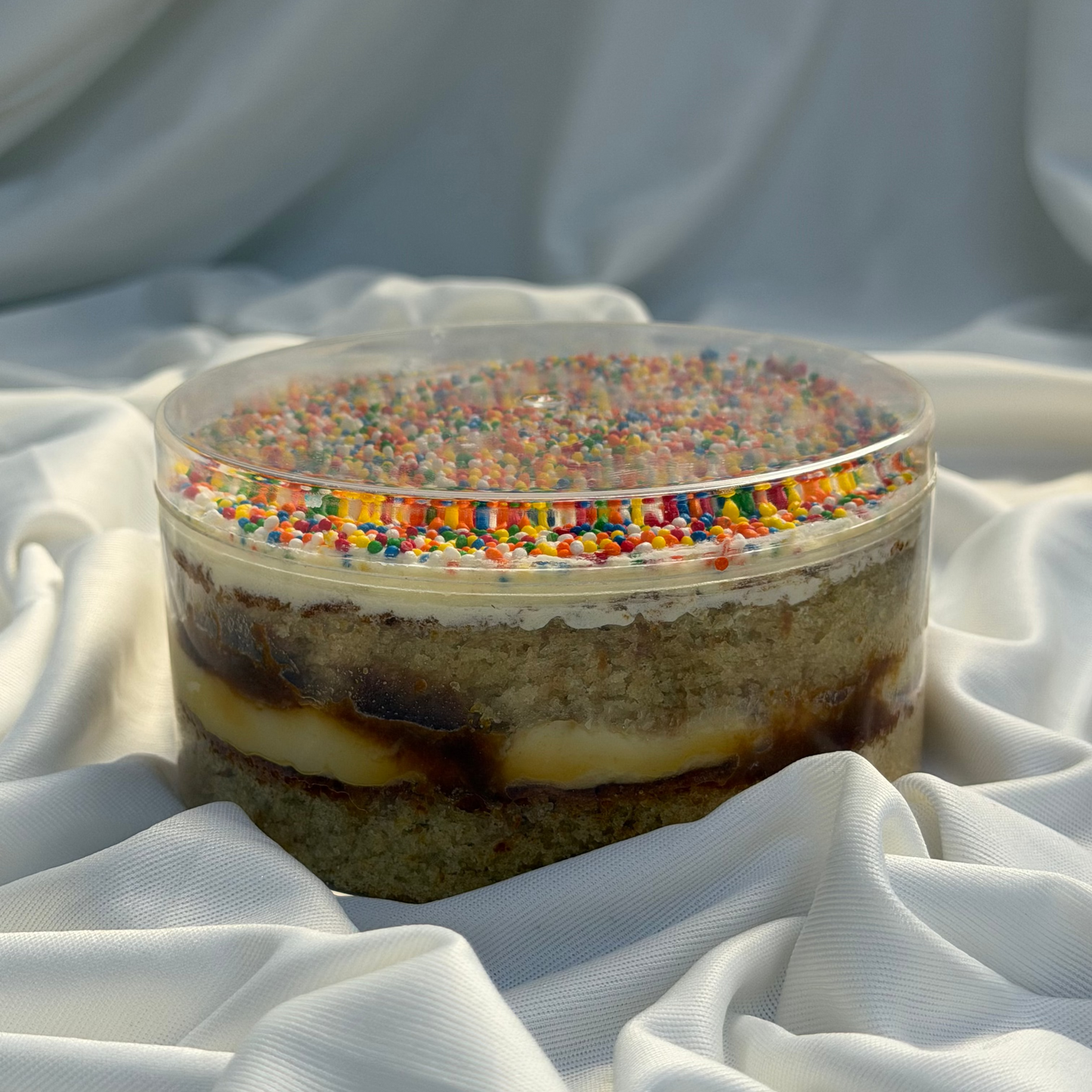 Layered dessert with colorful sprinkles on a white fabric background