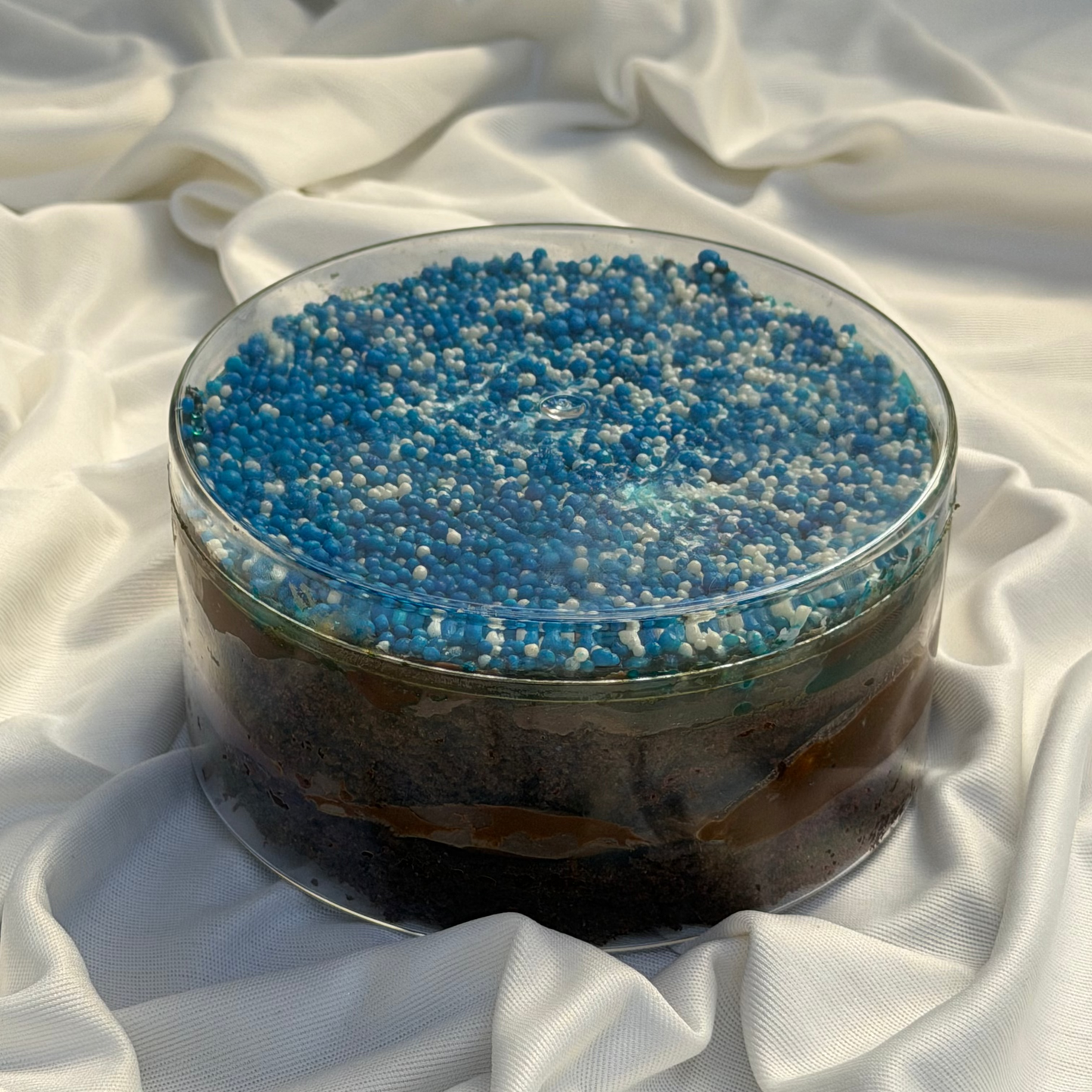 Glass bowl with blue and white dot cake on a white fabric background
