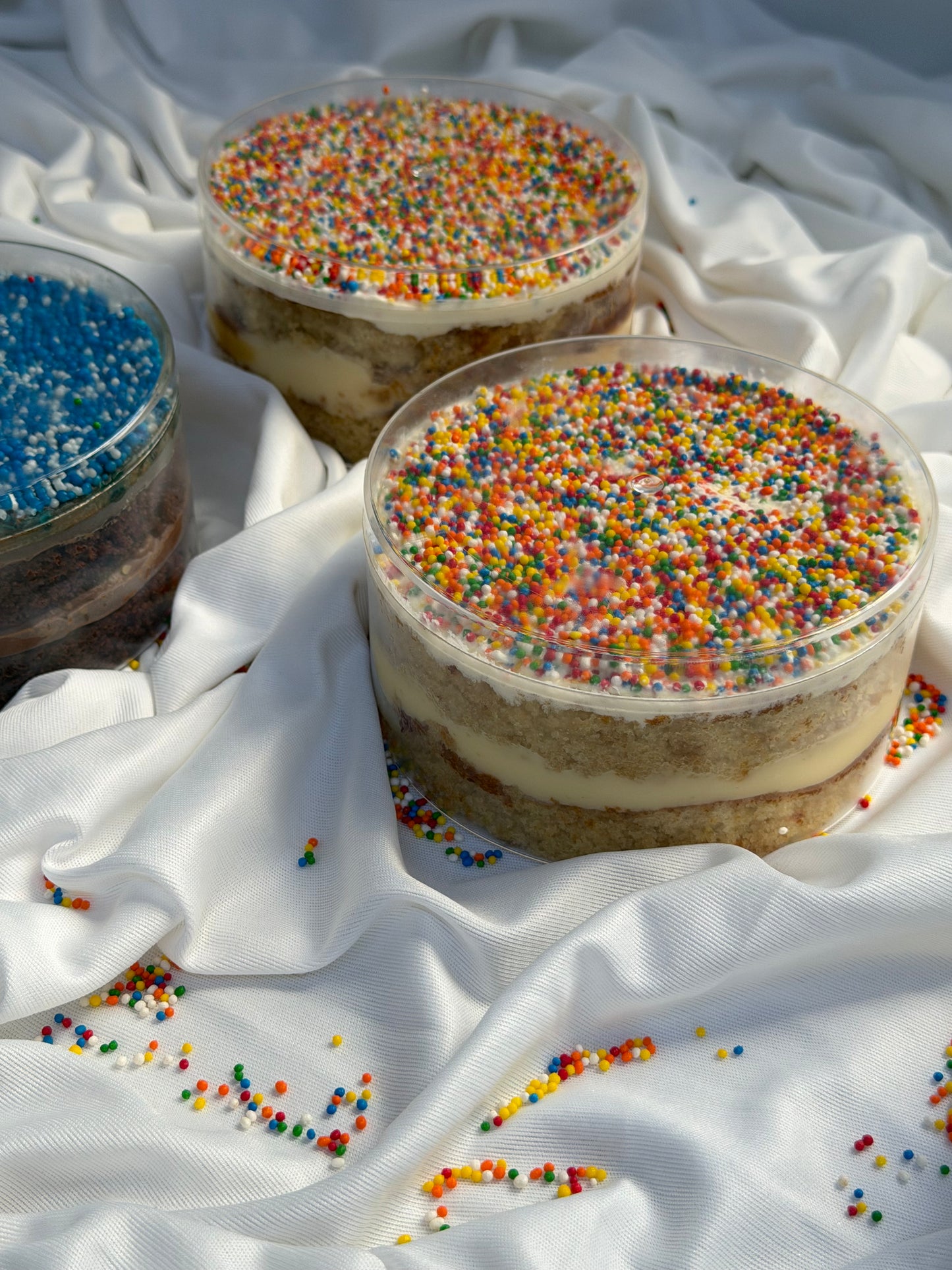 Two layered dot cakes with colorful sprinkles on a white fabric background