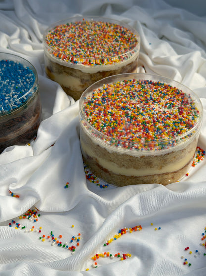 Two layered dot cakes with colorful sprinkles on a white fabric background