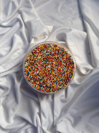 Round container filled with colorful sprinkles on a white fabric background