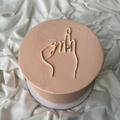 Round pink object with hand gesture design on a white fabric background