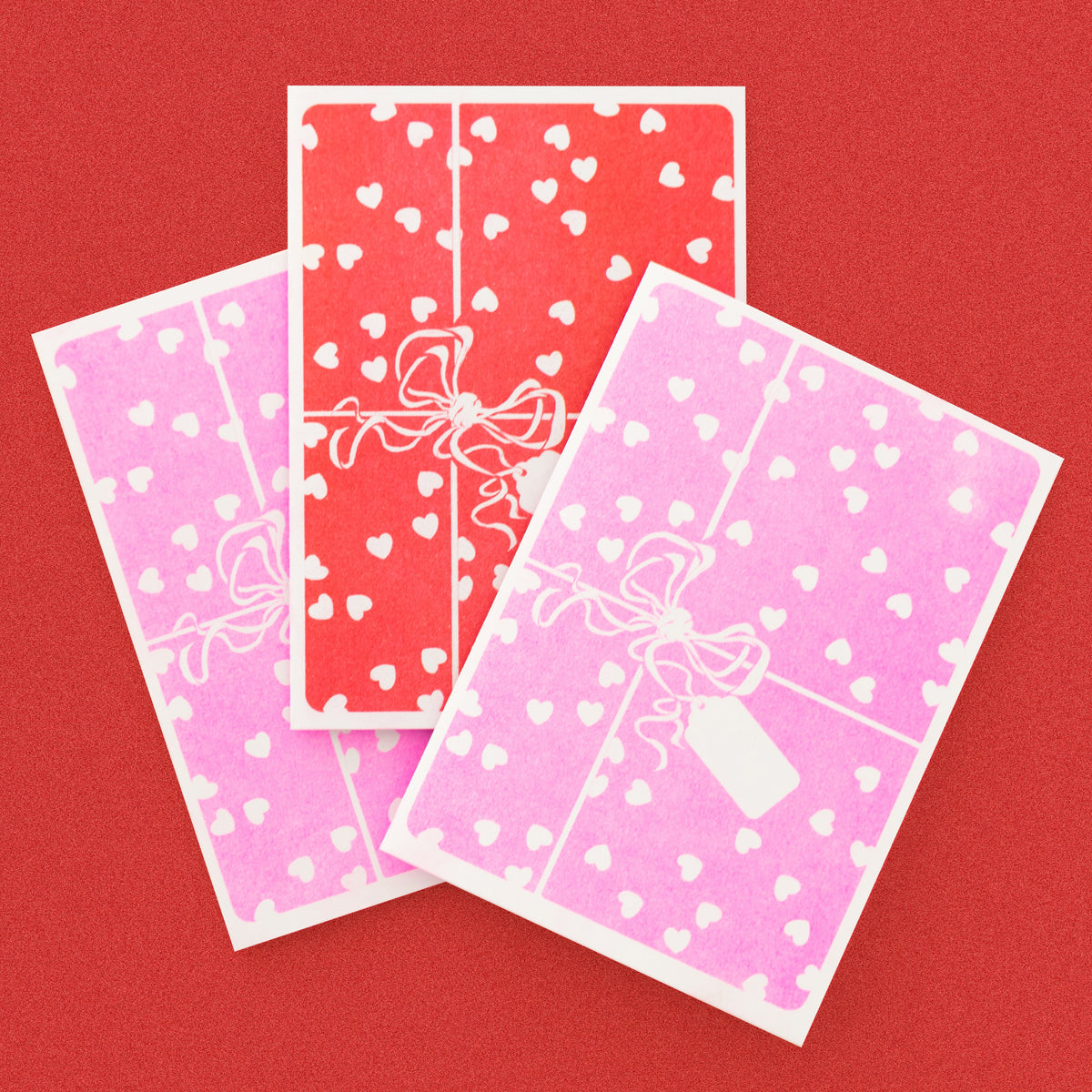 Three decorative paper sheets with heart and bow designs on a red background