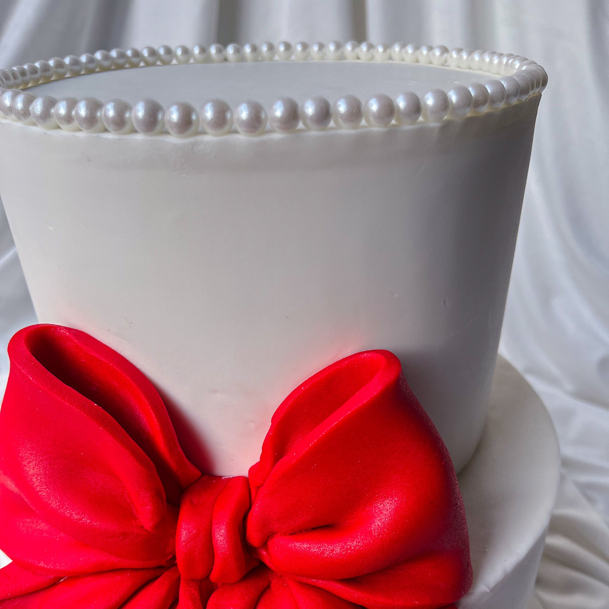 White cake with a red bow and pearl-trimmed top