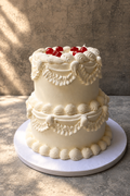 Two-tiered wedding cake with decorative icing and red berries on a neutral background