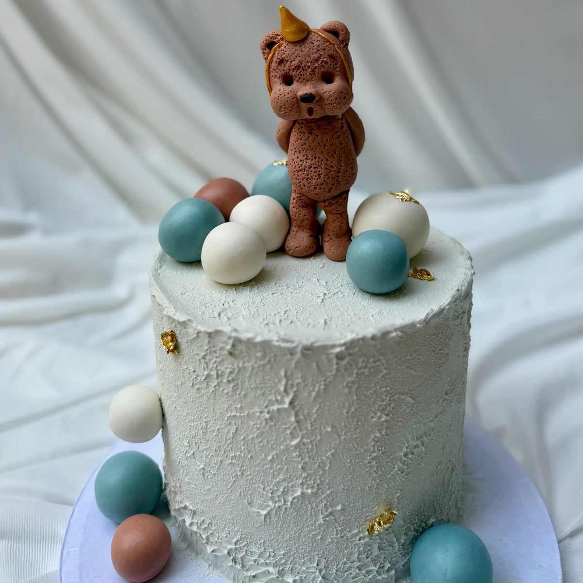 Small cake with a teddy bear topper and colorful balls on a white background