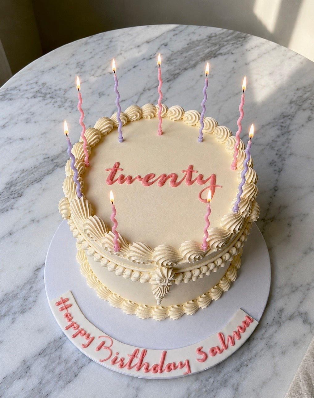 One-layer birthday cake with 'twenty' candles on a marble surface